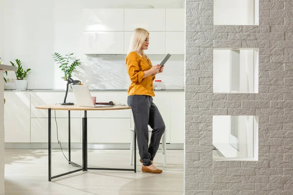 Jonge vrouw zitten in de keuken en werken op laptop. — Stockfoto