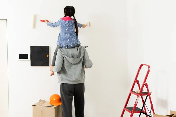 Glad ung familj renovera sitt hem, måla en vägg med en färg roller, mamman står på stegen och ler — Stockfoto