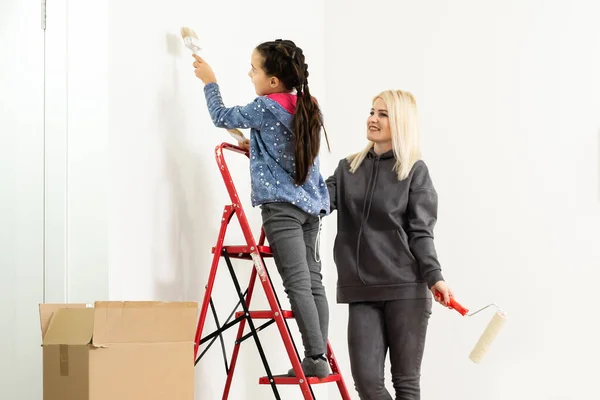Jovem família feliz renovando sua casa, pintar uma parede com um rolo de tinta, a mãe está de pé na escada e sorrindo — Fotografia de Stock