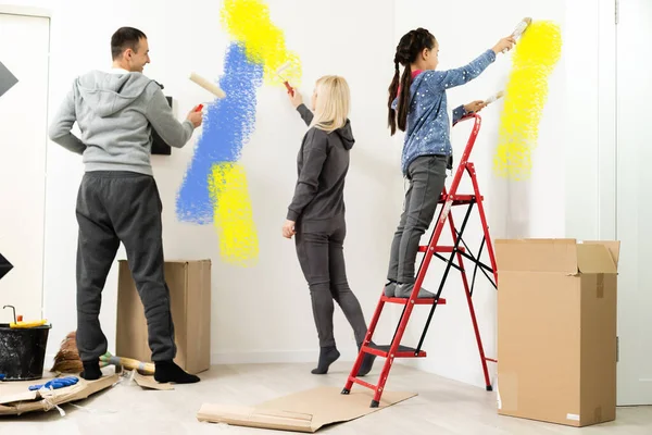 Reparación en el apartamento. Feliz familia madre, padre e hija hija pintan la pared con pintura — Foto de Stock