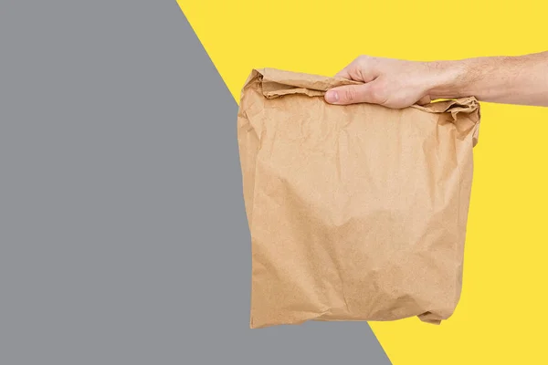 Cerrar hembra sostiene en mano marrón claro vacío vacío bolsa de papel artesanal para llevar Concepto de servicio de entrega. Copiar espacio. Colores de moda 2021 - Gris y Amarillo. — Foto de Stock
