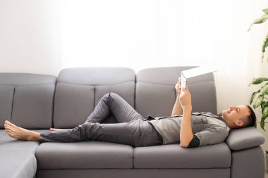 Evdeki kanepede oturan mutlu genç adam dizüstü bilgisayarda çalışıyor, gülümsüyor..