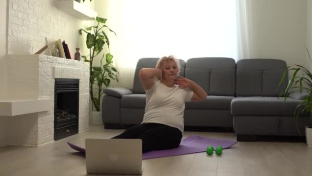 Ev sporu. Aktif kıdemli kadın dizüstü bilgisayarın önünde ısınma egzersizleri yapıyor, çevrimiçi öğretmenlerle eğitim görüyor. — Stok video