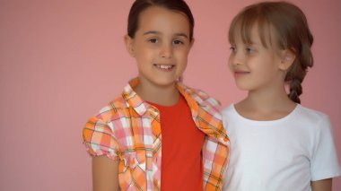 Pembe arka planda birbirini kucaklayan iki mutlu kız.