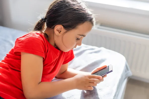 education, school, technology and internet concept - little student girl with smartphone at home