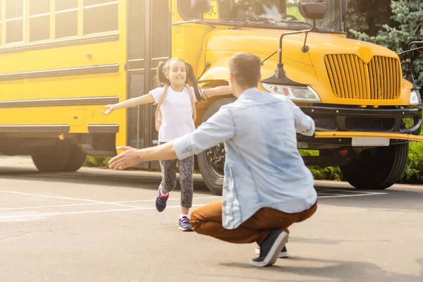 Отец встречает маленькую дочь, выходящую из школьного автобуса — стоковое фото