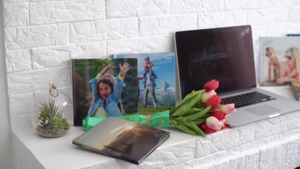 Laptop na białej półce z kwiatami. tulipany, fotoksiążka. — Wideo stockowe