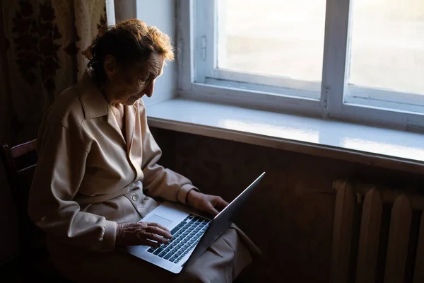 La donna anziana usa il portatile. Sembra molto sorpresa. Navigare in un browser e social media. Un portatile sul tavolo. Utilizzo della tecnologia nella vecchiaia — Foto Stock