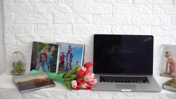 Laptop na białej półce z kwiatami. tulipany, fotoksiążka. — Wideo stockowe