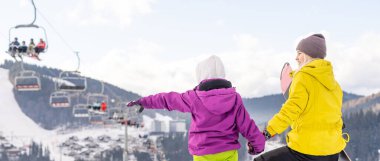 Anne ve kızı kış tatilinde snowboard yapıyor.
