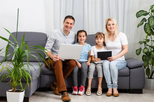 Ung glad avslappnad familj med två barn och par sitter på soffan och tittar på rolig video eller karikatyrer i touchpad — Stockfoto