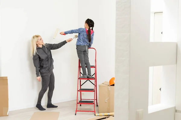 Mãe e filha felizes fazem reparos em casa. Sorrindo mulher e menina pintura na parede no quarto — Fotografia de Stock