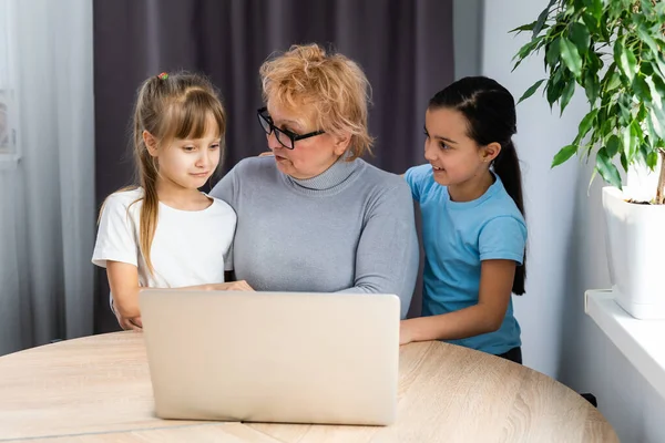 Nagymama és két unoka otthon használja a laptopot. — Stock Fotó