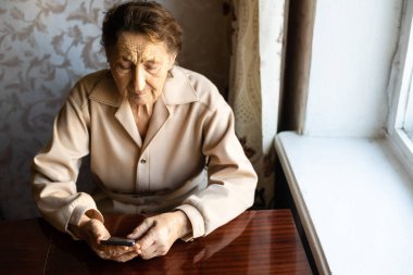 Çok yaşlı bir kadın evde akıllı telefon kullanıyor..