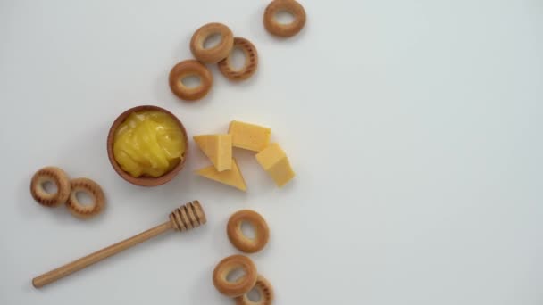 Honey in a wooden bowl, bagels and cheese on a white background — Stock Video