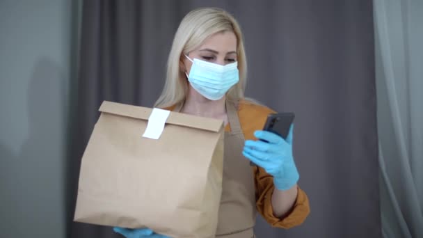 Ochrona zdrowia, bezpieczeństwo i koncepcja pandemii - kobieta w masce ochronnej twarzy i rękawicach trzymająca skrzynkę na paczki i na tle magazynu — Wideo stockowe