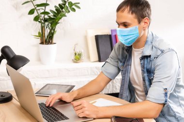 Koronavirüs salgını nedeniyle karantina. Evde kal. Evden çalışan bir iş adamı, koruyucu bir maske takıyor. Dezenfektan jeliyle evden çalış. Uzaktan çalışma, COVID-19 salgını nedeniyle öğrenme