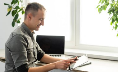 Gülümseyen genç serbest çalışan, dizüstü bilgisayar kullanan, online çalışan, evden çalışan, mutlu, bilgisayar başında yazan, internette sörf yapan, uzak işlerden keyif alan,.