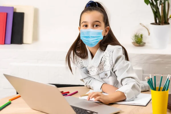 Κοριτσάκι με ιατρική μάσκα που σπουδάζει στο σπίτι. επιδημία, πανδημία — Φωτογραφία Αρχείου