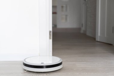 Beyaz robotik süpürge, oturma odasının iç tarafındaki plastik zeminde toz temizliyor. Akıllı ev idaresi teknolojisi.