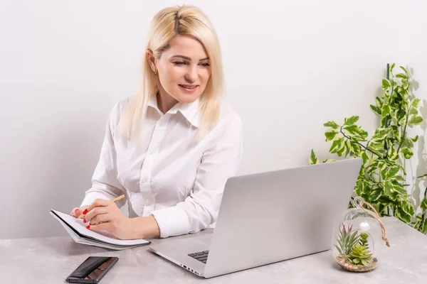Щаслива молода красива жінка використовує ноутбук, індори на фоні білої стіни — стокове фото