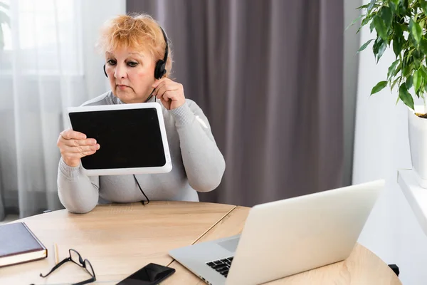 Sonriendo moderna madura 60s mujer caucásica en auriculares ver webinar en línea en casa. Feliz padre de pelo gris hembra divertirse estudio en Internet. Concepto de tecnología de edad avanzada —  Fotos de Stock