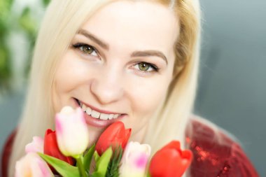 Evde anneler günü konseptinde elinde lale buketi tutan genç bir kadın yakından gülümsüyor.