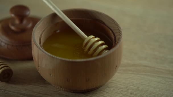 Miel con tarro de miel de madera en cuenco de madera sobre mesa de madera — Vídeos de Stock