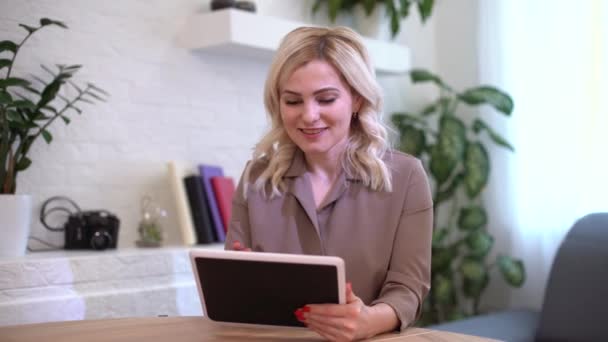 A happy woman girl works remotely from home and communicates via video call with friends and relatives in her office. Distance learning and work online. Using the tablet — Stock Video