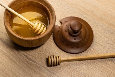 Koyu ahşap bir kasede bal, kırsal ahşap bir tabak. Tahta kaşık yavaşça damlıyor..