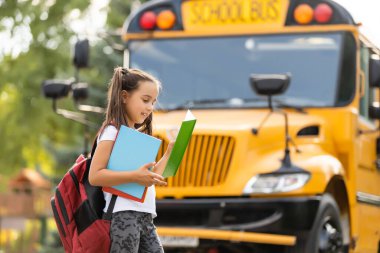 Sarı okul otobüsünün yanında sırt çantalı bir kız. Öğrenciler için taşıma