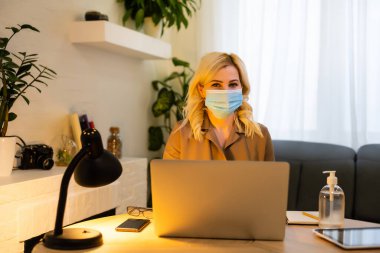 Ofiste. Yüz maskeli kadın, dezenfektan masanın yanında duruyor.