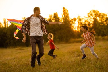 Mutlu aile babası ve kızı çayır üzerinde bir uçurtmayla koşuyor