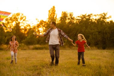 Mutlu aile babası ve kızı çayır üzerinde bir uçurtmayla koşuyor