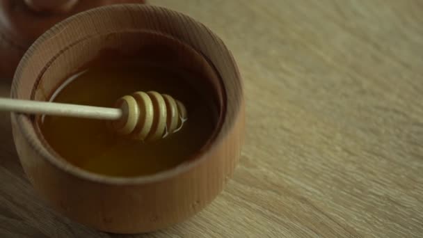 蜂蜜滴，从蜂蜜调酒师倒在木碗里。特写。健康的有机厚蜂蜜从木制蜂蜜勺浸出，特写镜头。4K UHD视频镜头。慢动作 — 图库视频影像