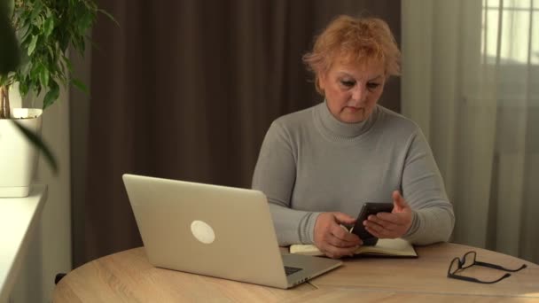 Ouderen die thuis aan een laptop werken. Portret van een oudere zakenvrouw die thuis belt en op afstand op de computer werkt — Stockvideo