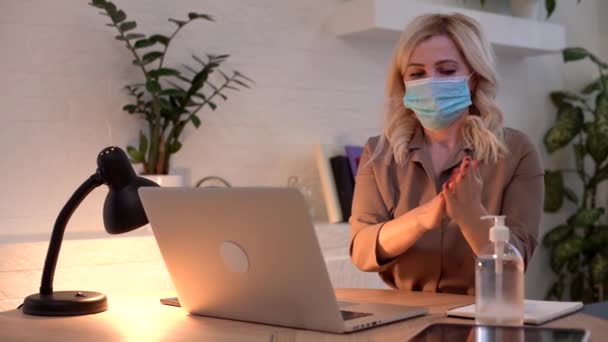 Schützen Sie sich während einer Pandemie, einer Epidemie. Junge Frau im Büro sprüht Desinfektionsmittel auf ihre Hände, eine medizinische Maske auf ihre — Stockvideo