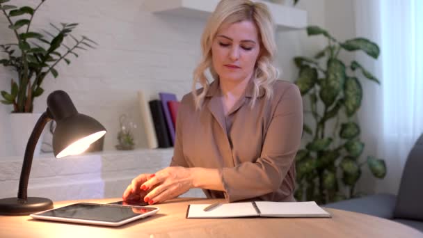 Pozytywna biała kobieta biorąca długopis i spisująca biznes plan. Portret młodego krawca siedzącego w pracowni z maszyną do szycia na stole. Mała przedsiębiorczość. — Wideo stockowe