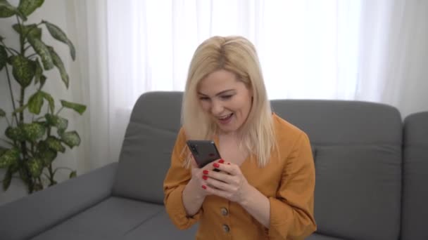 Portret van een gelukkige zakenvrouw geniet van succes op mobiele telefoon op kantoor. Sluiten vrolijke meisje lezen goed nieuws op de telefoon in slow motion. Verrast dame viert overwinning op de telefoon in appartement. — Stockvideo