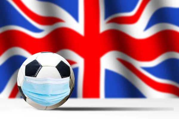Soccer ball in a medical mask against the background of the uk flag. Corona protection against viruses bacteria stop. Cancellation of sporting events. Copy space