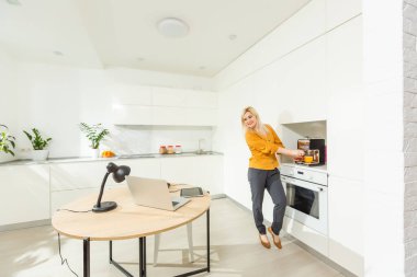 Uzaktan kumanda evden çalışıyor. Laptop kullanan genç bir kadın. Mutfak ofisinde serbest çalışan bir işyeri. Tecrit edilmiş telgraf, kadın işi, internetten alışveriş. Uzaktan öğrenme öğrencisi. Yaşam tarzı anı.