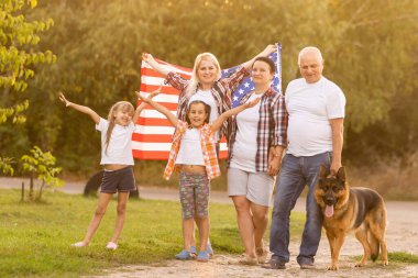 Büyük aile ayaklı Amerikan bayrakları taşıyor. Ön manzara, parktaki çayırdaki Amerikalı vatanseverler..
