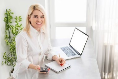 Dizüstü bilgisayarı olan genç bir kadın not defterine yazıyor.