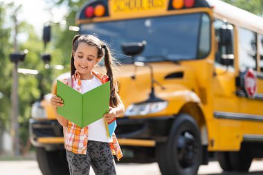 Okul otobüsünün yanındaki sevimli küçük kız ve kameraya bakıyor.