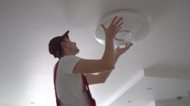 Elektrikçi iş başında. Elektrik kablolarının tamiri ve tavan lambalarının değiştirilmesi için servis. Bir müteahhit çatı katı tarzı ahşap bir tavan kuruyor. Kiralık centilmen ev işlerine yardım ediyor.