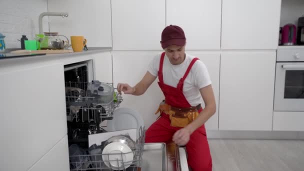 Mutlu efendi. Erkek teknisyen bulaşık makinesinin yanında elinde tornavidayla oturuyor. — Stok video
