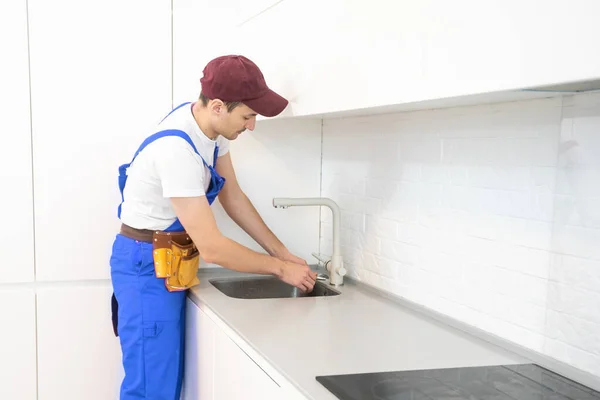 Lächelnder erwachsener Reparateur mit Schraubenschlüssel repariert Wasserhahn in der Küche — Stockfoto