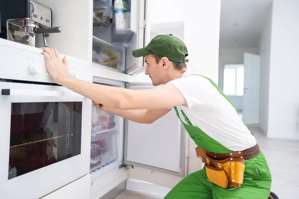 Schöner junger Reparateur, der mit einem Schraubenzieher den Ofen repariert — Stockfoto