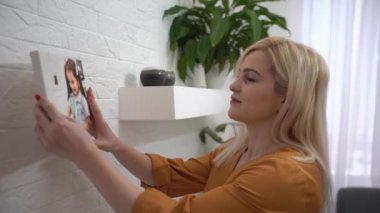 Yandan bakan mutlu genç kadın şömineye fotoğraf koyuyor, oturma odasını dekore ediyor. Gülümseyen kadın ev sahibi iç dekorasyondan zevk alıyor, evi rahat hale getiriyor. dokunaklı kavram. Kadınlar resim asar.