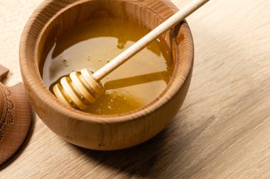 Koyu ahşap bir kasede bal, kırsal ahşap bir tabak. Tahta kaşık yavaşça damlıyor..